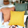 Warm tan, sage, and mustard farmhouse-style pillows on a white blanket – cozy home decor from Nest and Paw.
