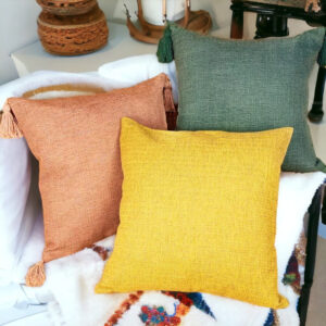 Warm tan, sage, and mustard farmhouse-style pillows on a white blanket – cozy home decor from Nest and Paw.